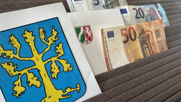 Das Bild zeigt die Wappen der Stadt Hagen und des Landes Nordrhein-Westfalen sowie Geldscheine unterschiedlichen Wertes. 